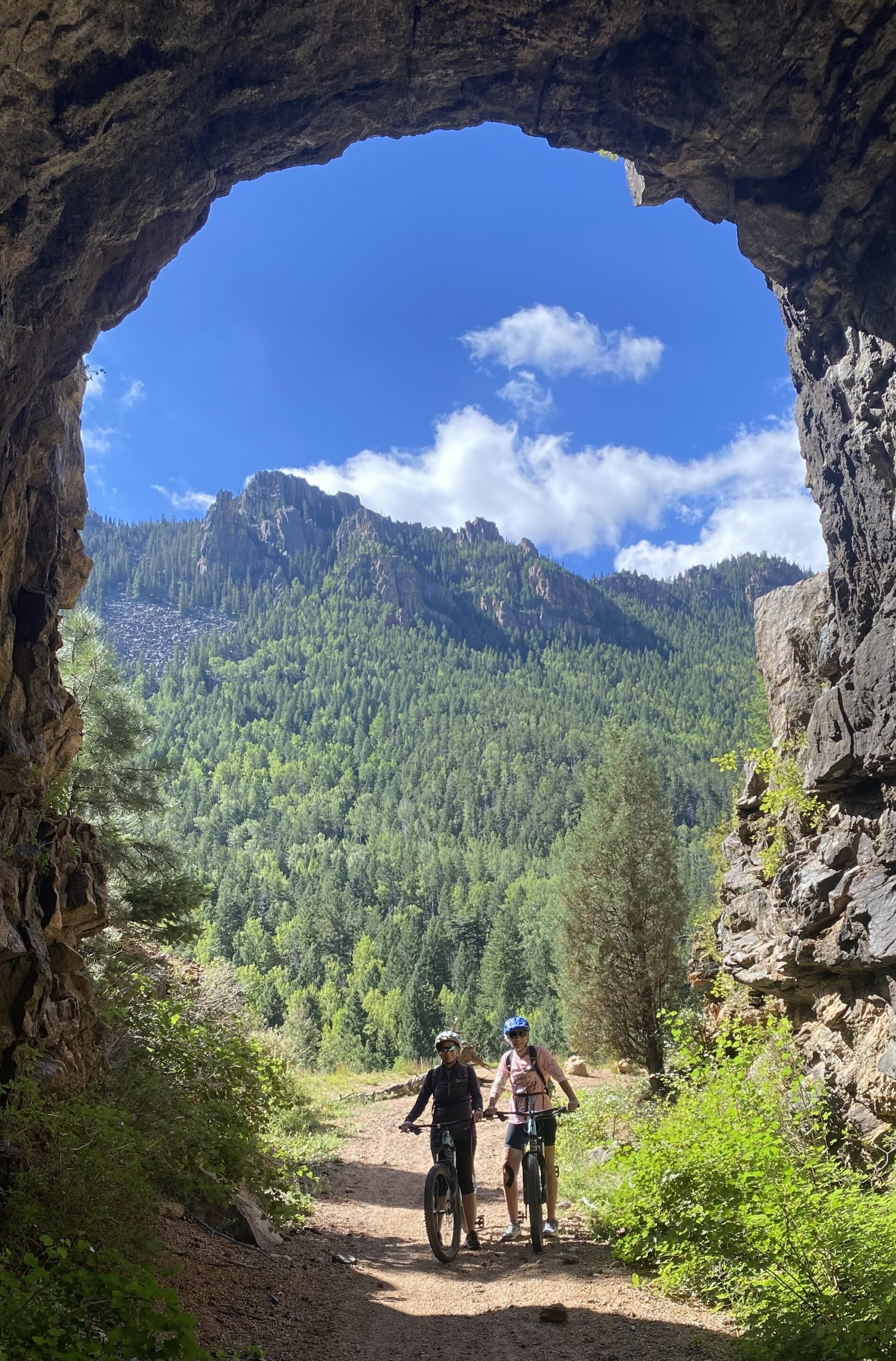 two bike riders in a tunnel with forested mountains behind