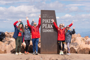 five people standing by the Pikes Peak summit sign cheering