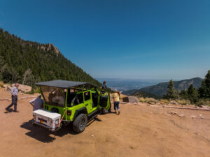 Group of people standing next to a green Jeep with a scenic overlook