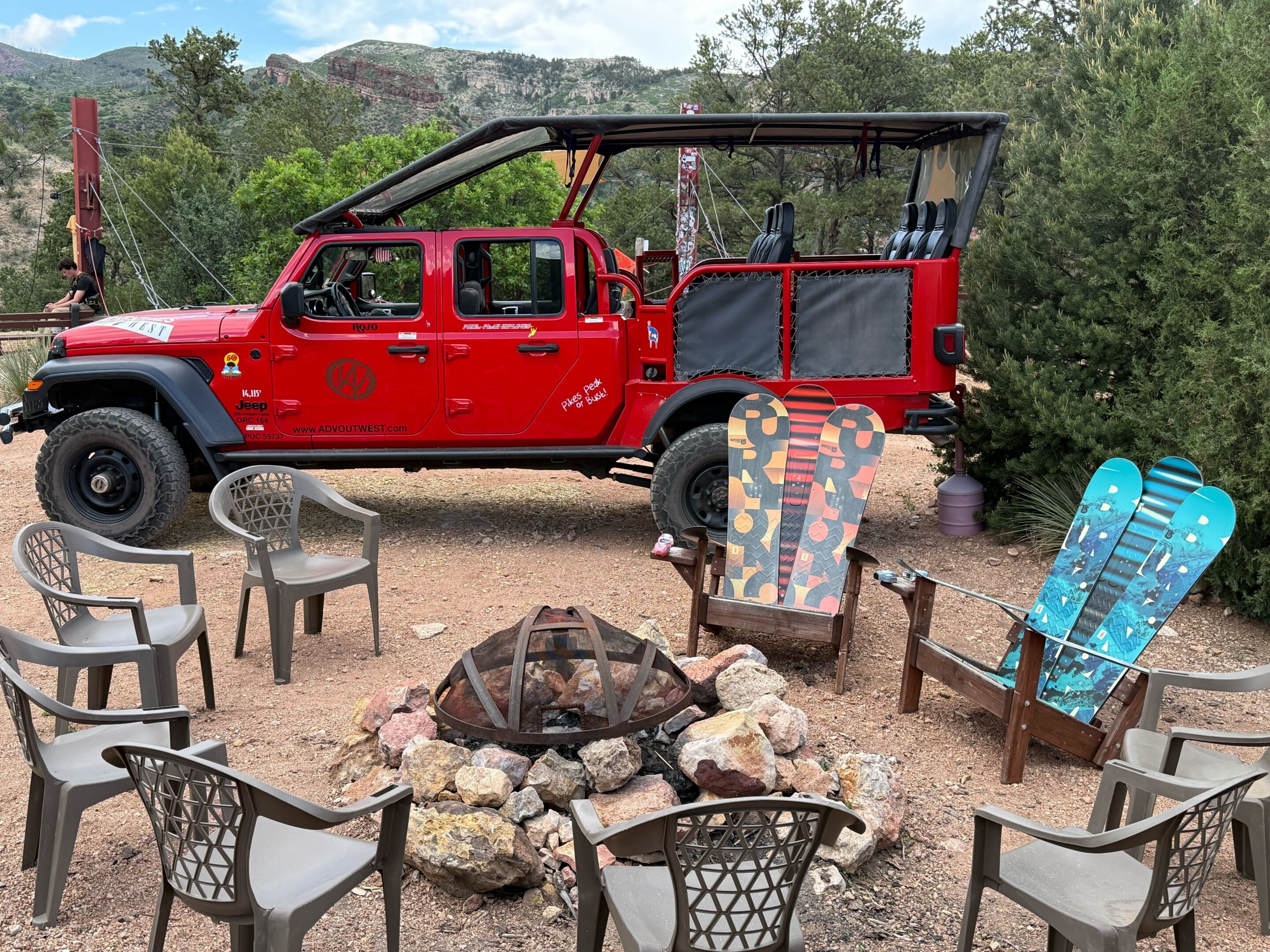 Red Jeep next to mountain campfire and seating
